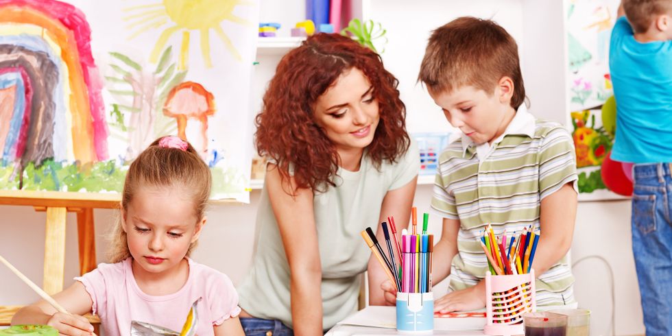 Das Bild zeigt eine Erzieherin und drei Kindern beim Basteln in einem Aufenthaltsraum