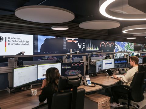 Büro des Bundesamt für Sicherheit in der Informationstechnik. Zwei Mitarbeitende sitzen an ihren Arbeitsplätzen vor mehreren Bildschirmen.