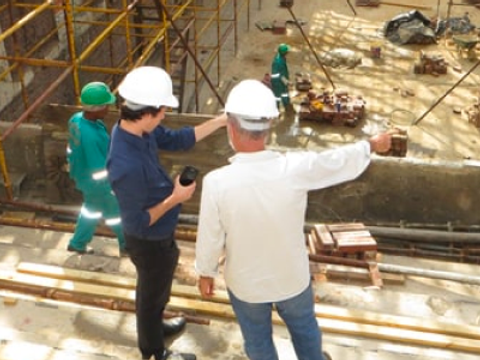 Zwei Arbeiter befinden sich auf einer Baustelle, stehen auf einem Gerüst und beraten sich.