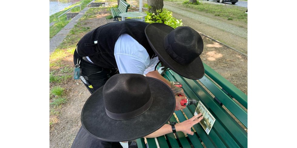 Zimmerleute bringen eine Plaktette auf der renovierten Bank an