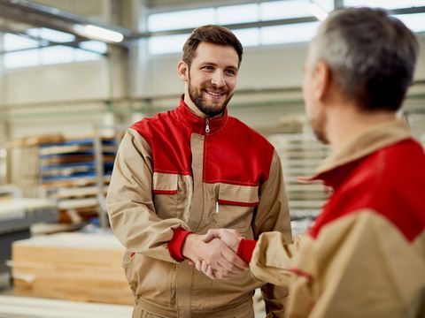 2 arbeitende Personen geben sich freundlich die Hand in einem Werk.