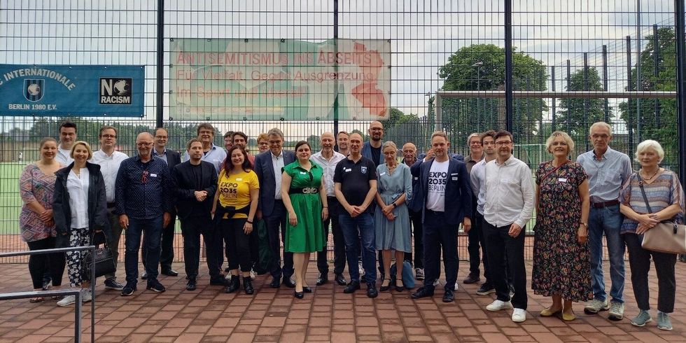 Gruppenfoto auf einem Sportplatz vor einem Fußballfeld