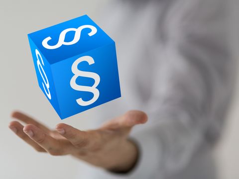Eine Hand wirft einen blauen Würfel mit weißem Paragraphen zeichen hoch