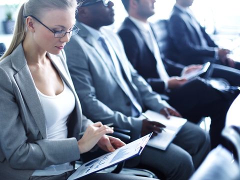 4 Menschen als Zuhörer, Frau ganz vorne mit Notizen in der Hand