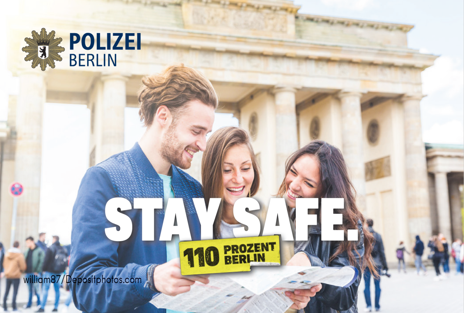 Personen mit einer Karte vor dem Brandenburger Tor darüber Schriftzug Stay Safe 110 Prozent Berlin