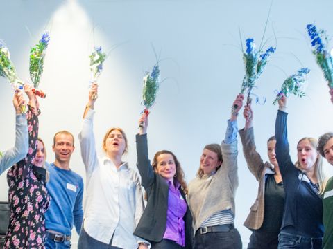 Die Teilnehmer*innen des K+-Führungskräfteprogramms halten Blumensträuße in die Luft