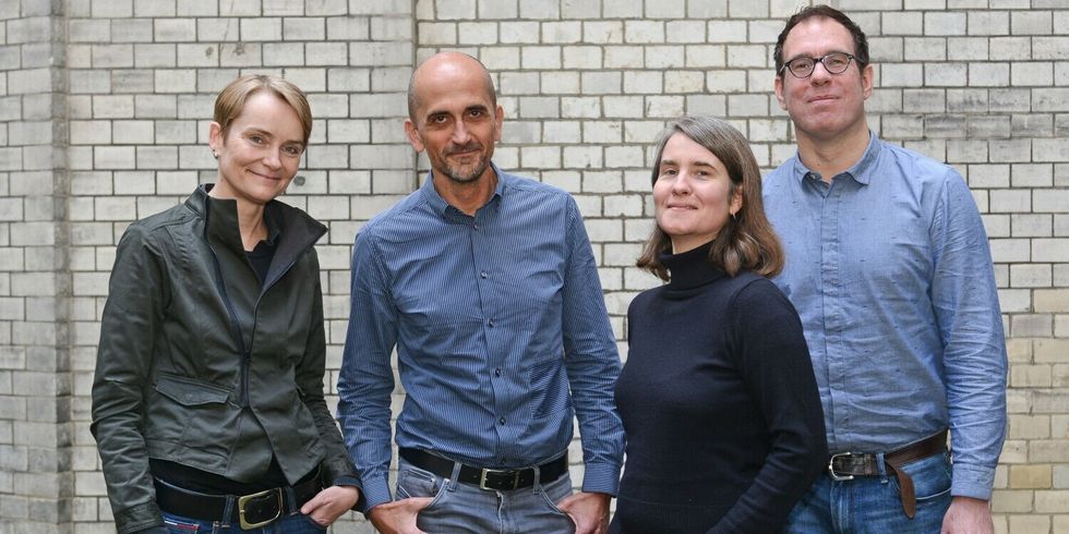 Vier Personen stehen zusammen vor einer gemauerten Wand und lächeln in die Kamera.