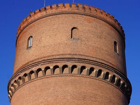Ziegelstein-Wasserturm mit Rundbogenfries und Zinnen vor blauem Himmel
