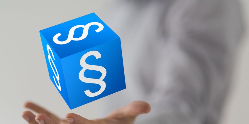 Eine Hand wirft einen blauen Würfel mit weißem Paragraphen zeichen hoch