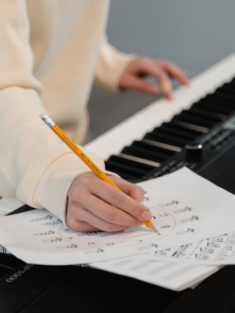 Person spielt am Klavier und macht sich Notizen zu Musiktheorie