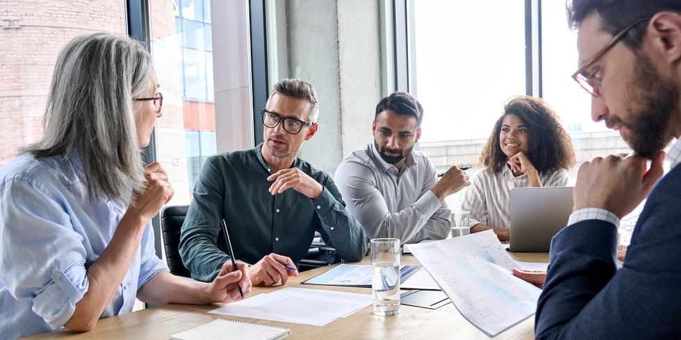 Fünf Menschen sitzen an einem Tisch und besprechen sich miteinander