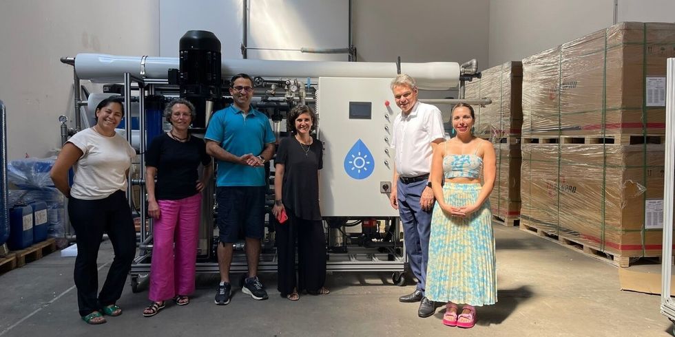 Sechs Personen stehen in einer Halle vor einer Maschine.
