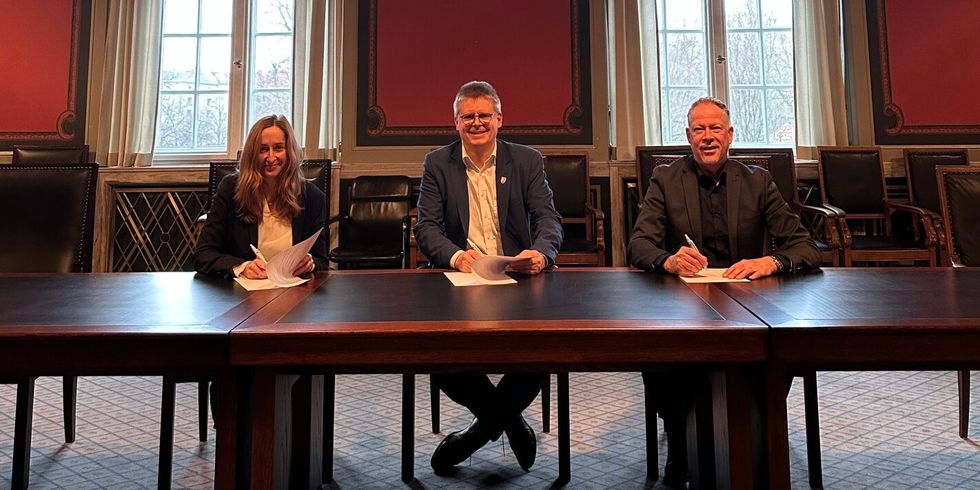 Drei Menschen sitzen nebeneinander an einem Tisch und schreiben auf Papier.