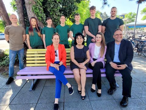 Probesitzen auf der Bank zum "Quasseltreff", vordere Reihe: Stadträtin Julia Schrod-Thiel, Bürgermeisterin Demirbüken-Wegner, Einsamkeitsbeauftragte Paris, Amtssteliter Sascha Braun; hintere Reihe Azubis des Straßen- und Grünflächenamtes, die mit geschickten Händen die Bank gestalteten. (Bild: BA Rdf)