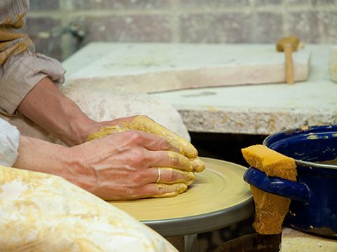 Kursszene - Hände halten gelben Ton auf der Drehscheibe