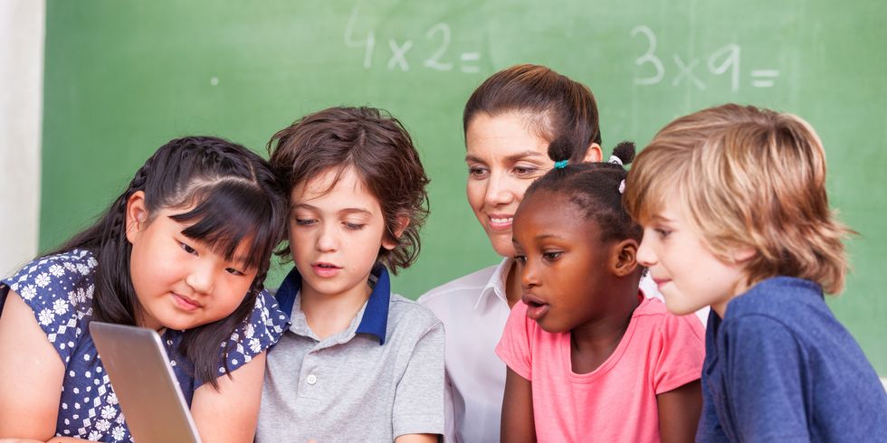 Schülerinnen und Schüler sitzen mit Lehrerin vorm Laptop