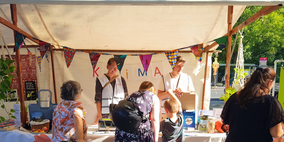 Das Bild zeigt einen Stand der Klimaleitstelle Reinickendorf. Davor stehen Menschen unterschiedlichen Alters und informieren sich im Gespräch mit den Mitarbeitern der Klimaleitstelle