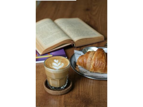 Blick auf einen Tisch mit einem aufgeschlagenen Buch, Milchkaffé und Croissant