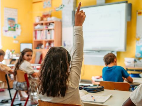 Kinder im Klassenzimmer. Ein Kind meldet sich im Unterricht