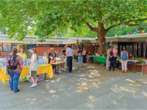mehrere Menschen besuchen Infostände in einem Innenhof mit einem Baum