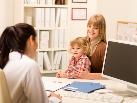Ein Kind sitzt auf dem Schoß seiner Mutter, die mit einer Kinderärztin spricht
