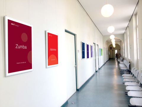 Heller Flur mit weißen Wänden und bunten Kursplakaten in der Volkshochschule Berlin Mitte, Lehrstätte Antonstraße.