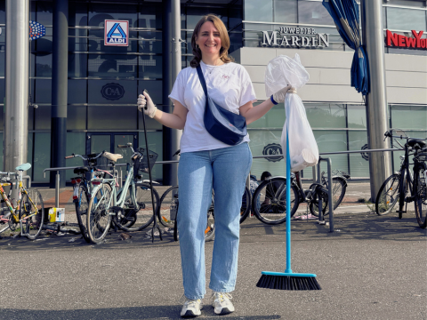 Eine Frau posiert mit Mülltüte, Besen und Zange auf der Straße