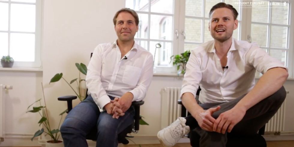 Gründer von Nia Health sitzen auf Stühlen und lachen in die Kamera