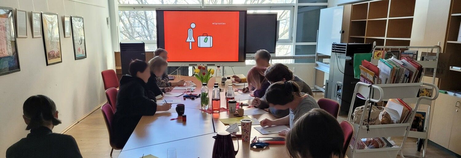 Tisch mit Menschen und Bildsdhirm mit Piktogramm