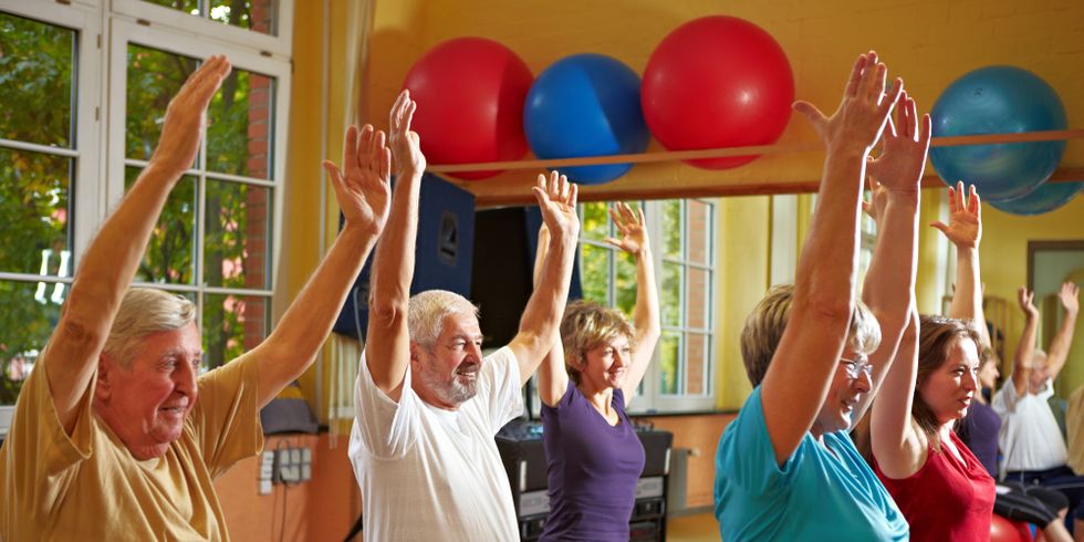 Eine Gruppe von Menschen verschiedenen Alters sitzen auf Gymnastikbällen und strecken die Hände in die Höhe.