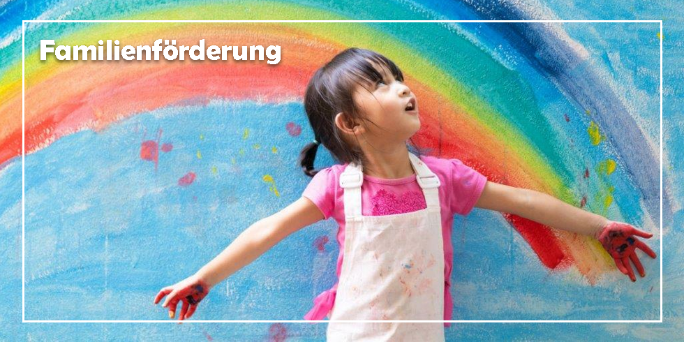 Ein Mädchen steht vor einer Wand, wo ein Regenbogen angemalt ist. Sie schaut mit offenen Mund nach oben.