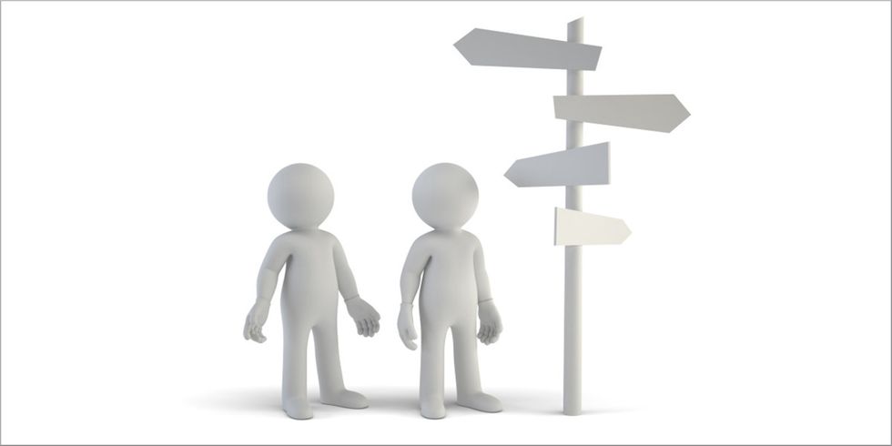 zwei abstrakte Figuren neben einem Wegweiser