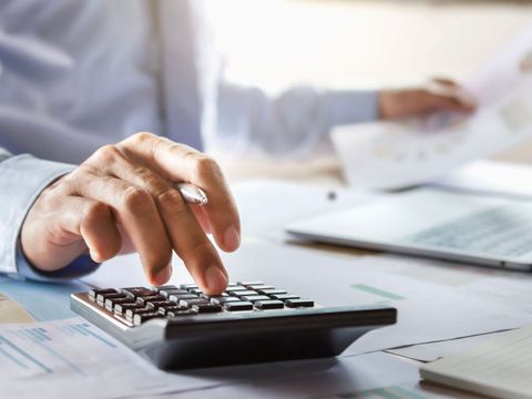 Ein Buchhalter arbeitet an seinem Schreibtisch und benutzt einen Taschenrechner, um einen Finanzbericht im Büro zu erstellen.