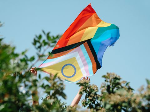 progressive pride flagge wird von zwei Händen gehalten vor blauem Himmel
