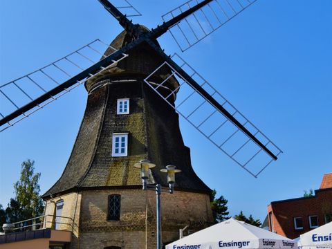 Windmühle mit einem dunklen oberen Teil aus Holz. Der untere Teil der Mühle besteht aus hellen Steinen