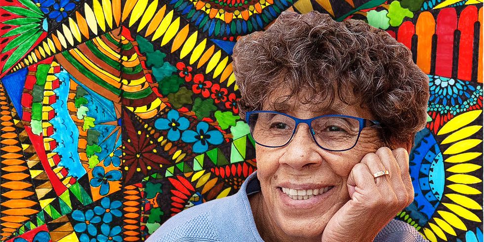 Eine lächelnde Frau mit Brille vor einem bunten Bild.