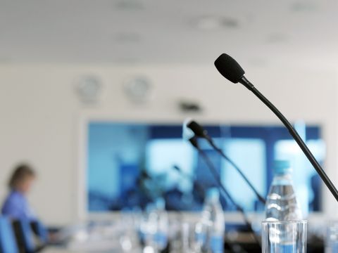 Konferenzraum mit Getränken im Vordergrund, mit Teilnehmenden im Hintergrund