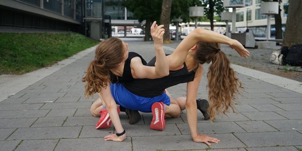 Zwei Frauen posieren aufeinander verhakt auf einem Gehweg.