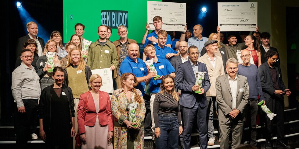 Auf den Treppen vor einer Bühne versammeln sich Personen für ein Gruppenfoto. Mehrere halten kleine Bären-Statuen oder Schecks in den Händen.