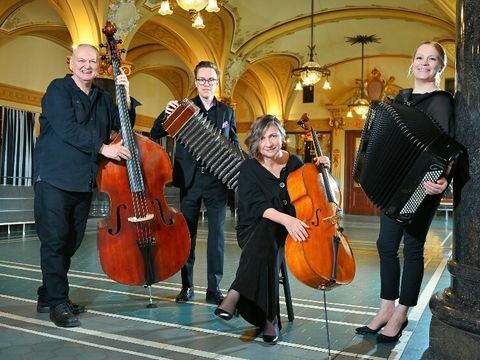 Vier Personen stehen zusammen mit Instrumenten in einer Halle.