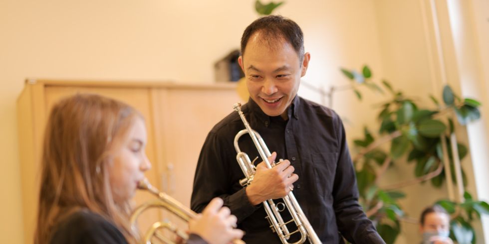 Bläserfestival der Musikschule City West: ein lächelnder Musiker mit Trompete in der Hand schaut einer jungen Trompeterin beim Spiel zu.