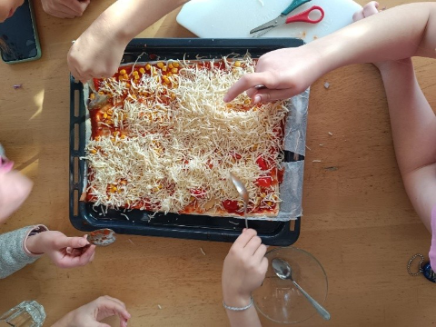 Hände die ein belegtes Pizzablech mit Käse bestreuen