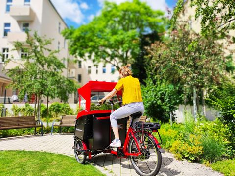 Mit dem Rücken zur Kamera gekehrte Frau fährt ein elektrisch unterstütztes Lastenfahrrad