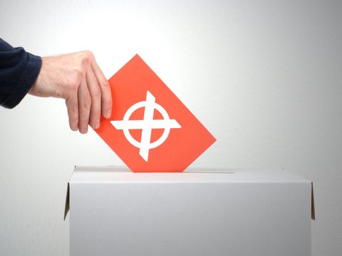 Hand, die einen Umschlag in eine Wahlurne steckt