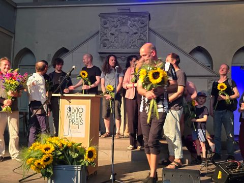 Werner Heck, Vorsteher der Bezirksverordnetenversammlung (Mitte) und Bezirksbürgermeisterin Clara Herrmann (re) gratulieren mit Sonnenblumen dem Gewinnerteam des Vereins "Suppe & Mucke" (Bild: Sabine Böhnig)