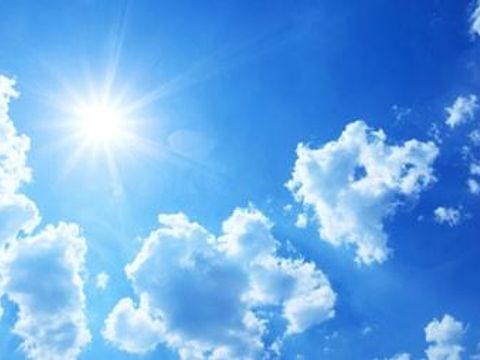 Sonne vor blauem Himmel umgeben von wenigen Wolken