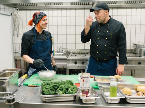 Eine Köchin und ein Koch stehen in einer Küche und probieren einen Dipp