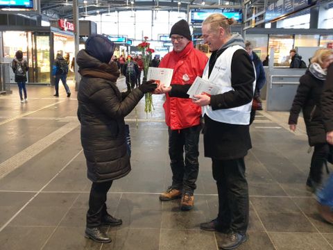 Bezirksstadtrat Nöll in weißer Weste verteilt DGB-Infoflyer und Blumen an eine Dame auf einem Bahnhof