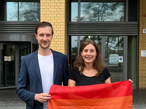 Bezirksbürgermeister Gordon Lemm und die QSF-Beauftragte Vanessa Krah stehen mit einer Regenbogenfahne vor dem Rathaus Marzahn-Hellersdorf. Im Hintergrund ist der Schriftzug "Rathaus" mit dem Bezirkswappen zu sehen