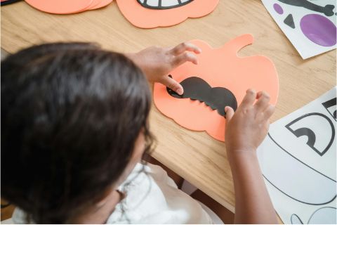 ein Kind klebt auf einen ausgeschnittenen Kürbis einen Schnurrbart